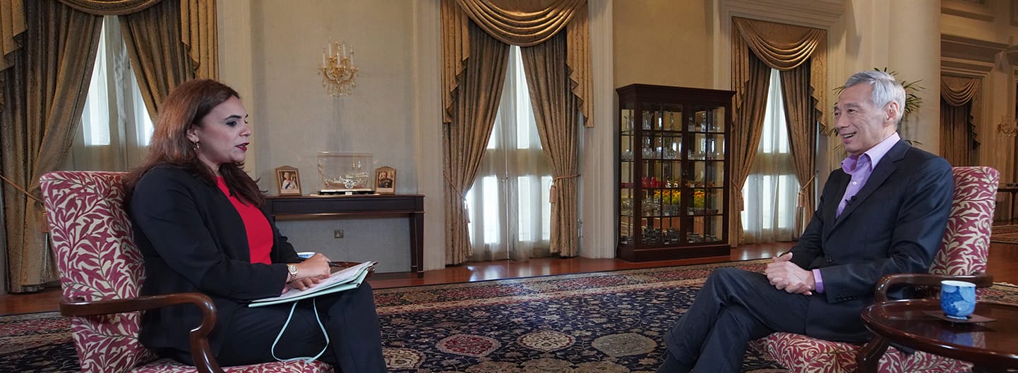 Woman interviews Lee Hsien Loong, both in suits, seated in ornate armchairs in a formal room.